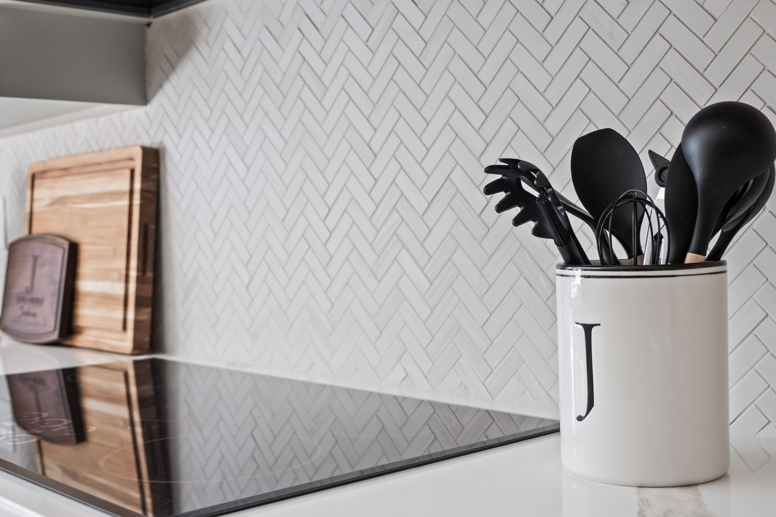 The herringbone tile backsplash behind a countertop utensil crock.