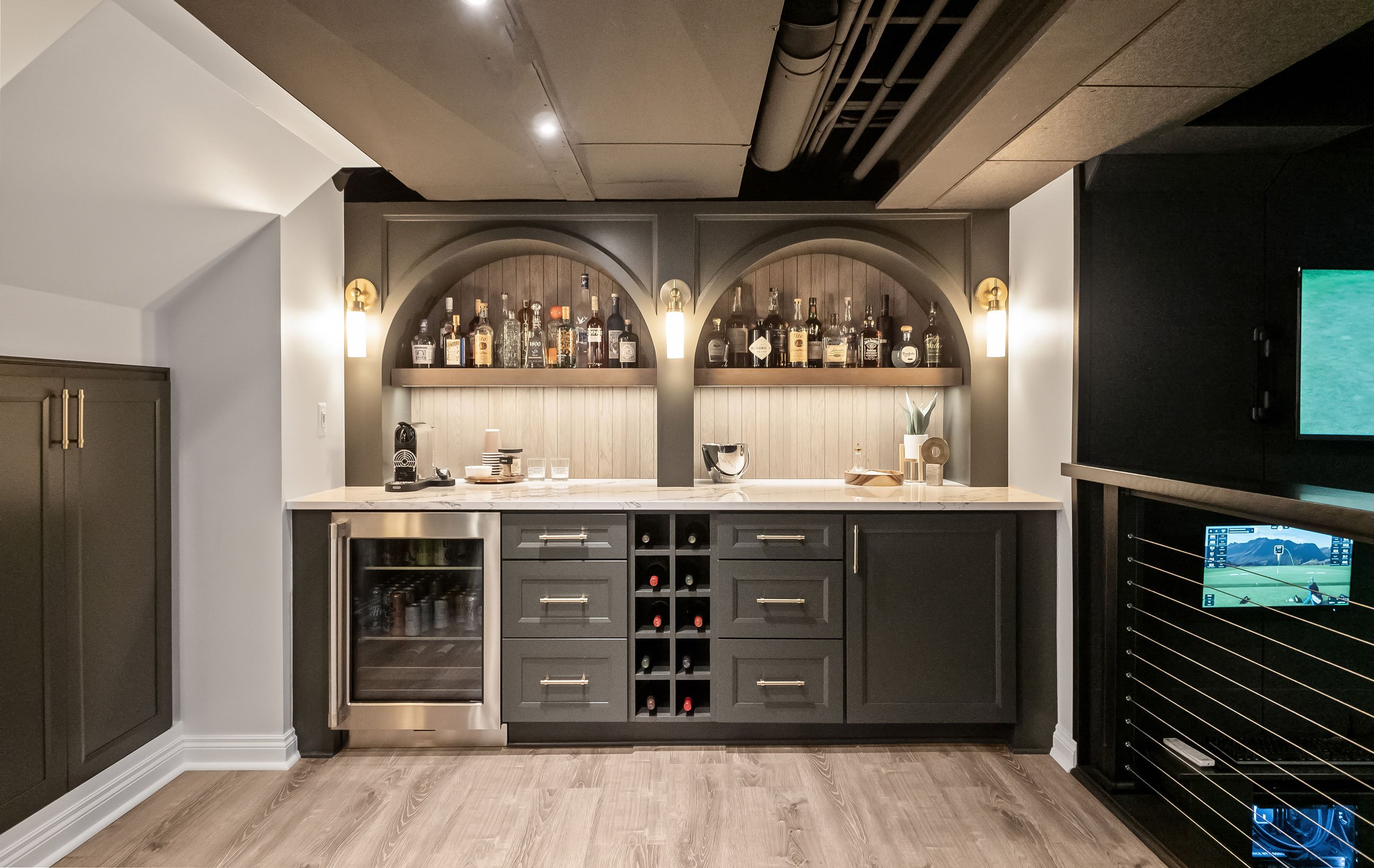 Custom basement bar with dramatic arches, green-veined quartz countertops, floating shelves, sconces, and moody speakeasy-inspired design.