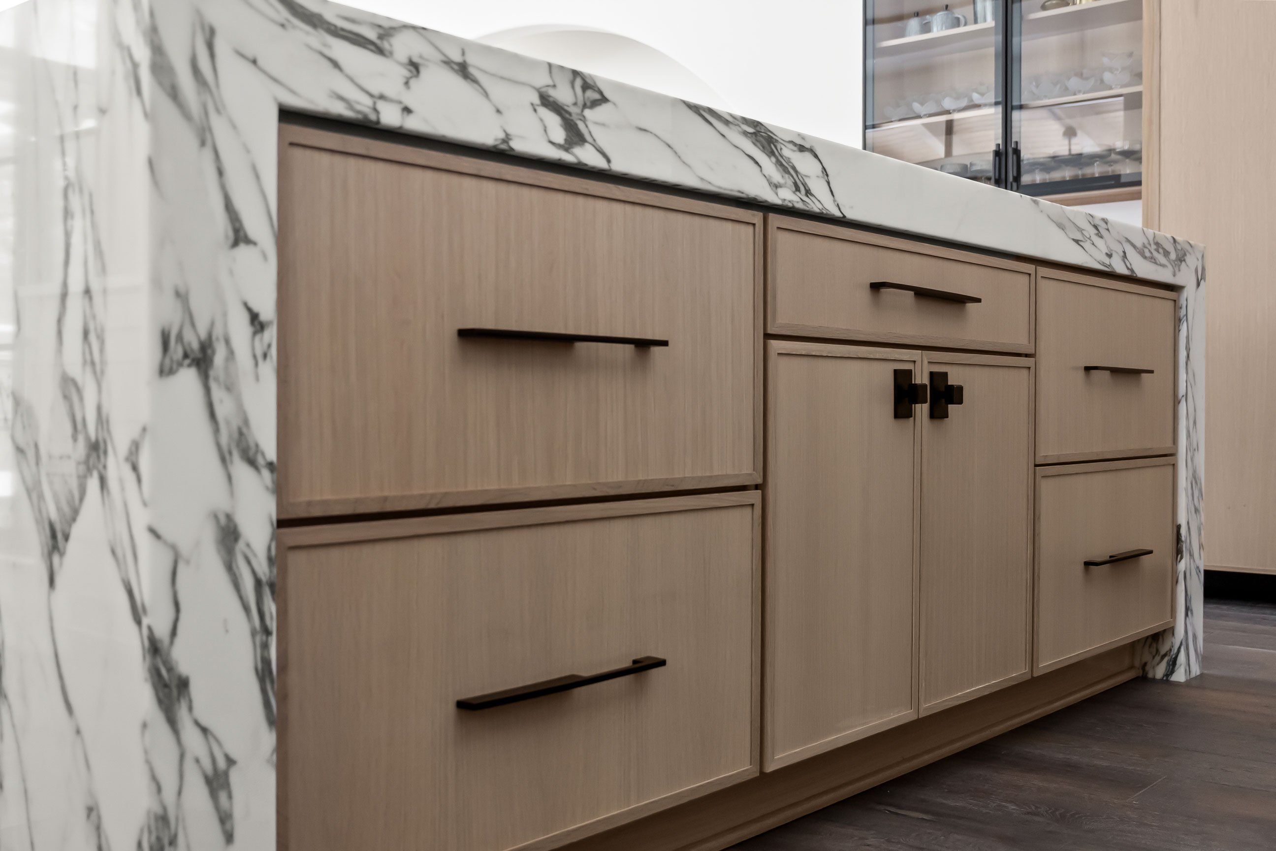 Spacious kitchen featuring quartersawn white oak cabinetry, metal-framed glass upper cabinets, and a large island with waterfall stone top.