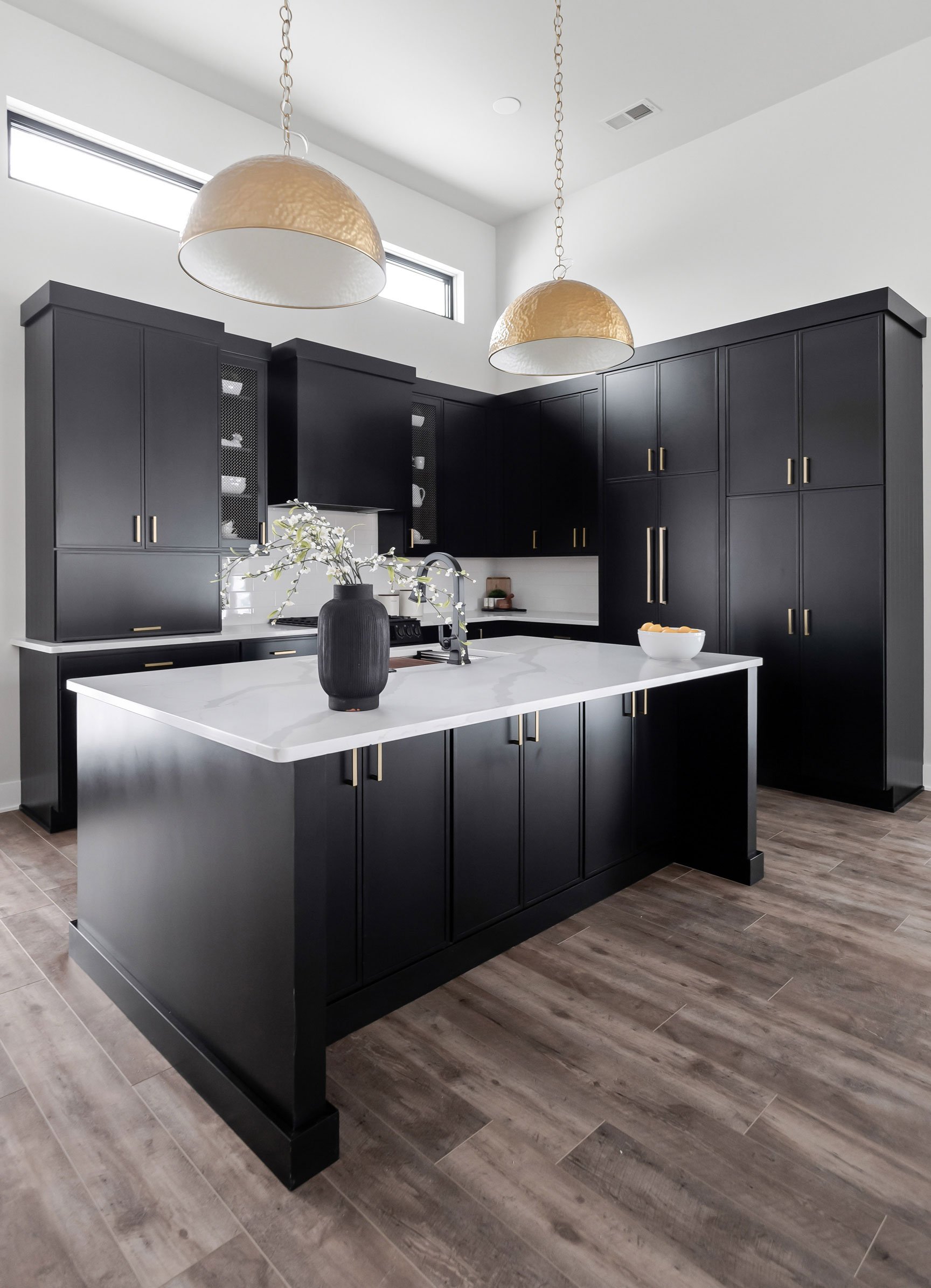 Dark moody kitchen with black slim shaker cabinets, gold pendant lighting, and white quartz island in barndominium
