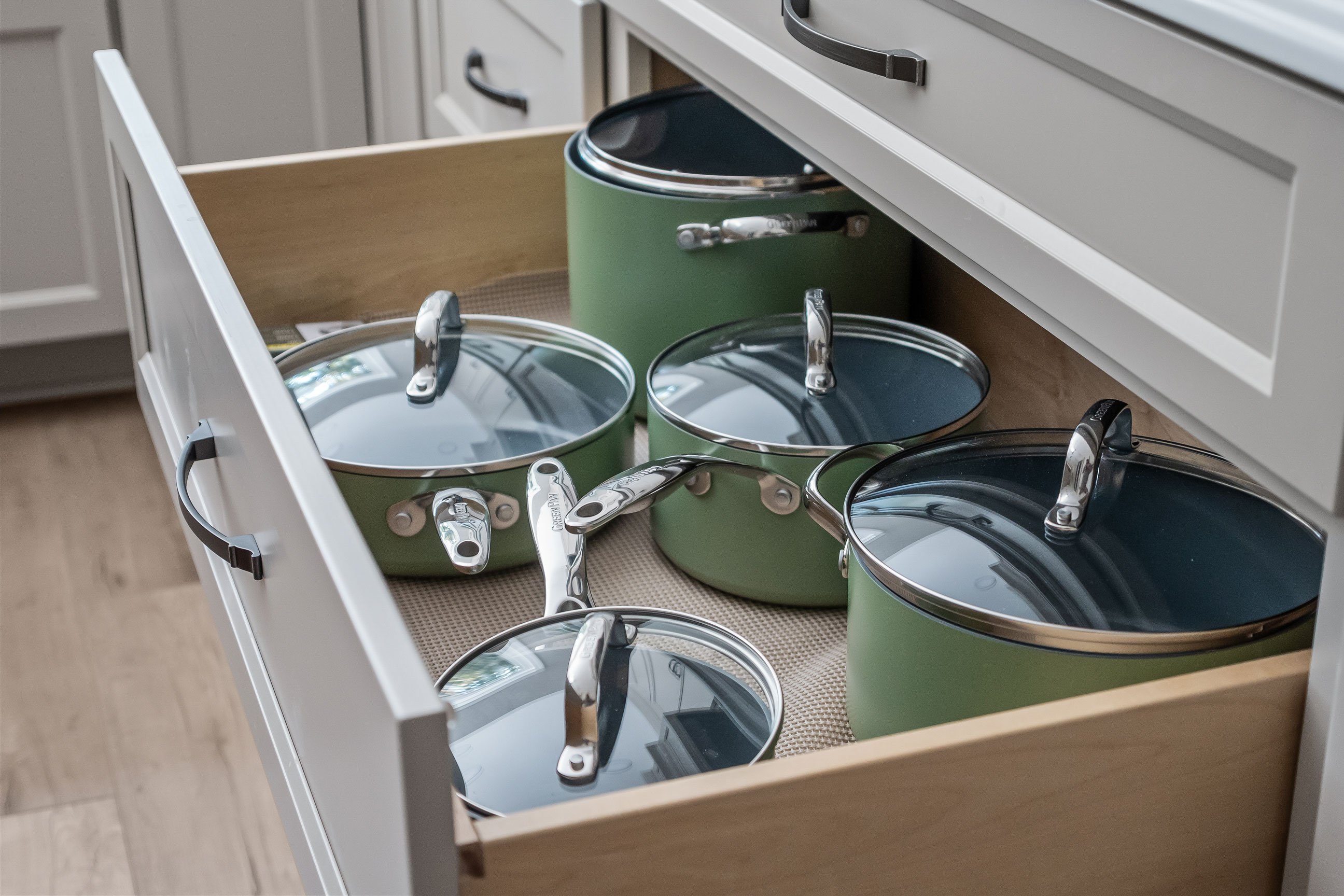 An open drawer showing a stacked set of green cookware with glass lids.