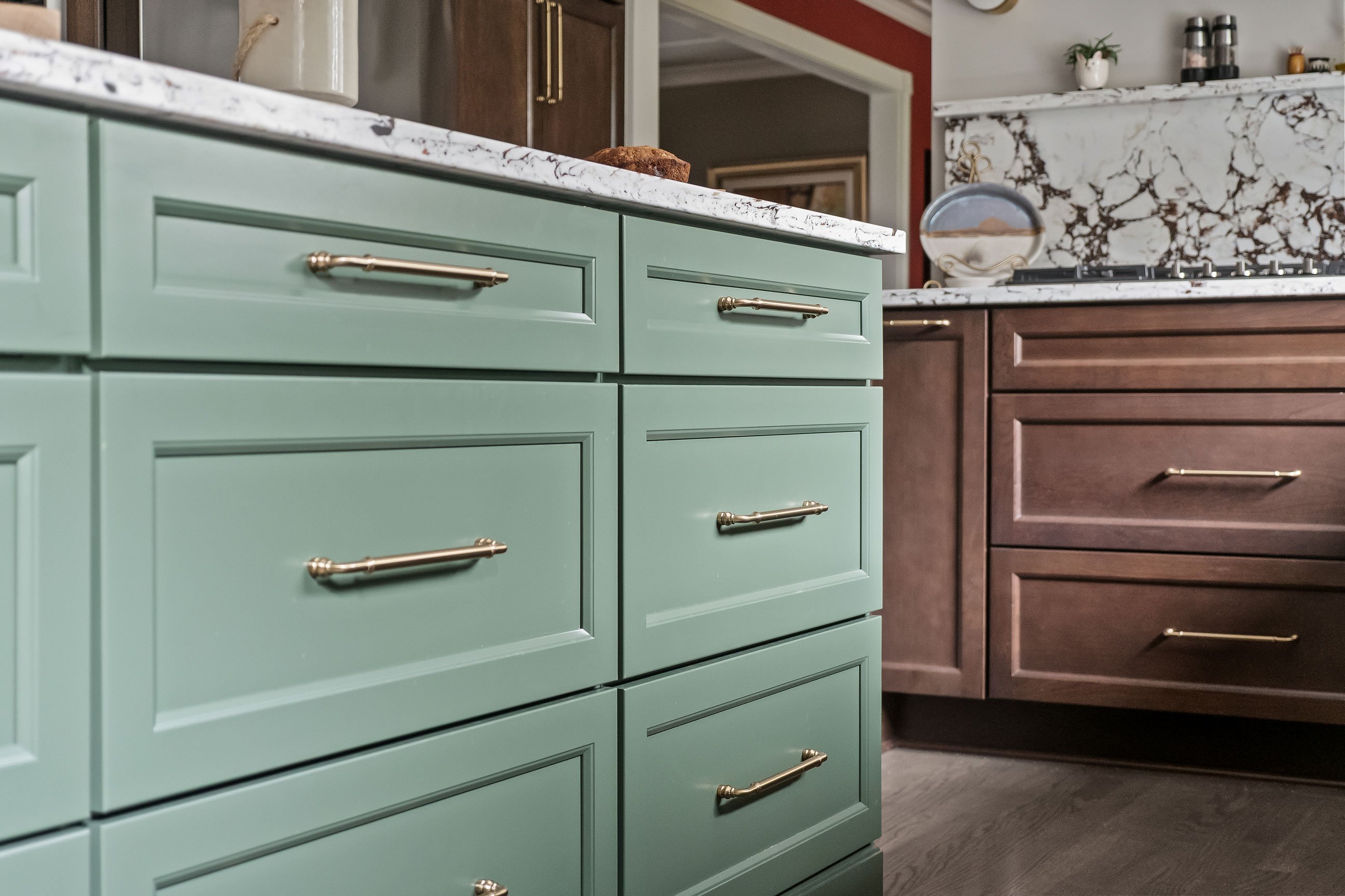 Close view of the green island's drawer fronts and gold hardware, with the range and cherry cabinetry in the background.