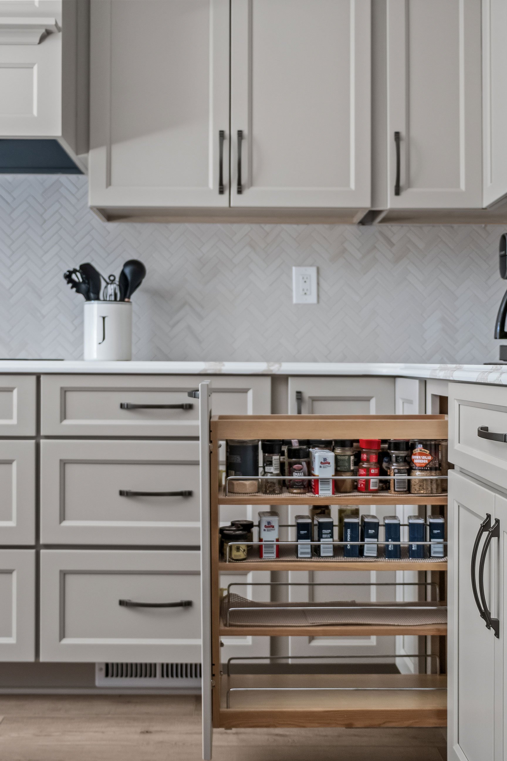 A pull-out spice rack drawer stocked with jars and seasoning bottles.