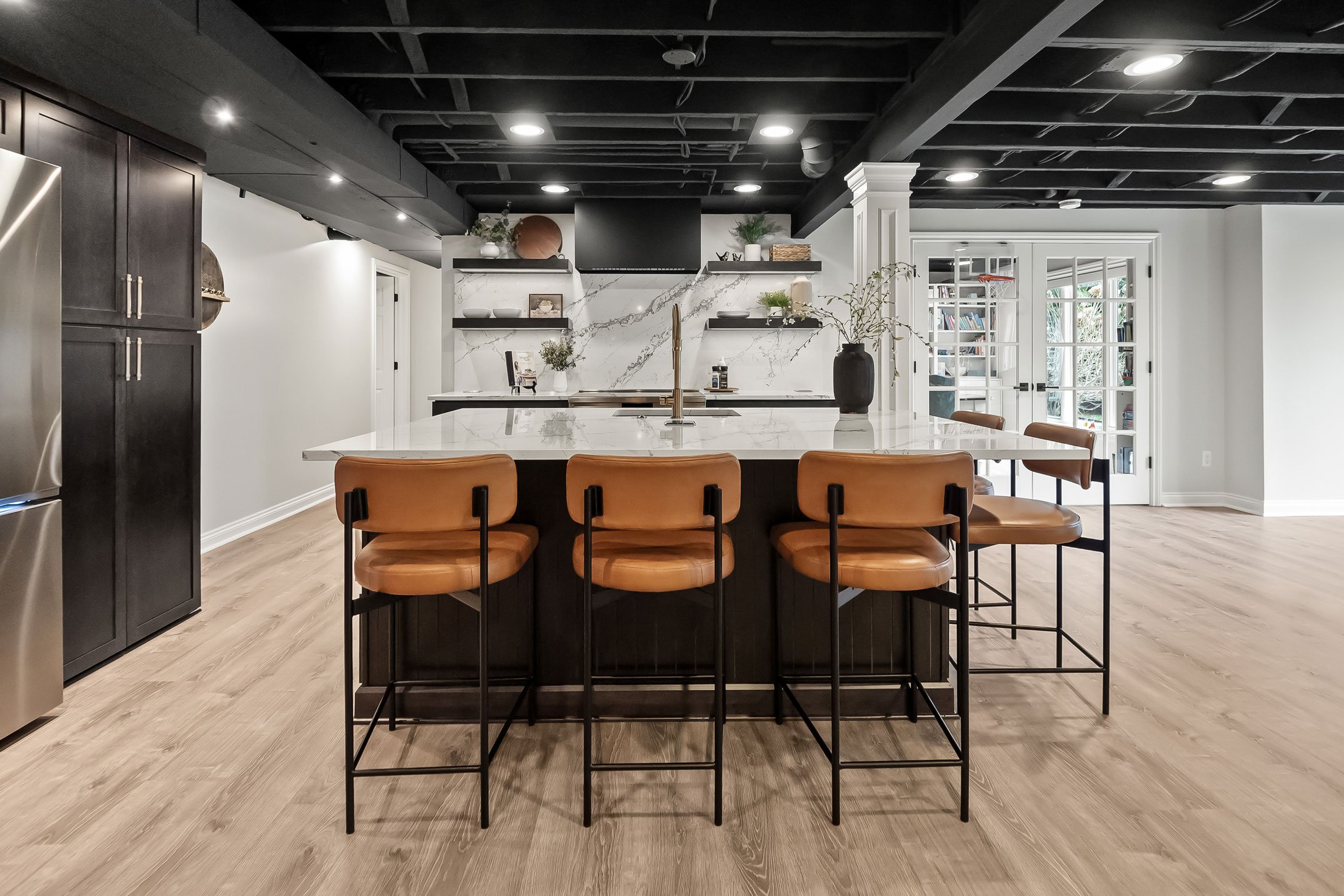 Basement entertainment kitchen with dark cabinetry, large island seating, quartz countertops, and open layout.