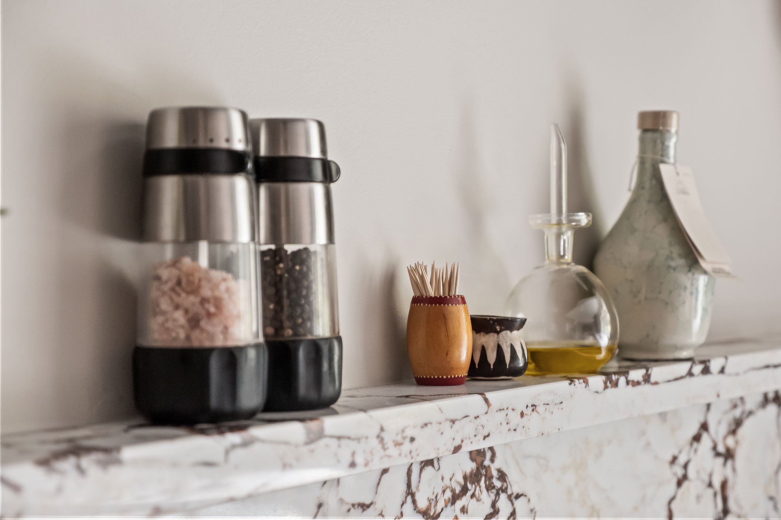 Detail of salt and pepper grinders, a toothpick holder, and oil bottles displayed on the stone backsplash shelf.