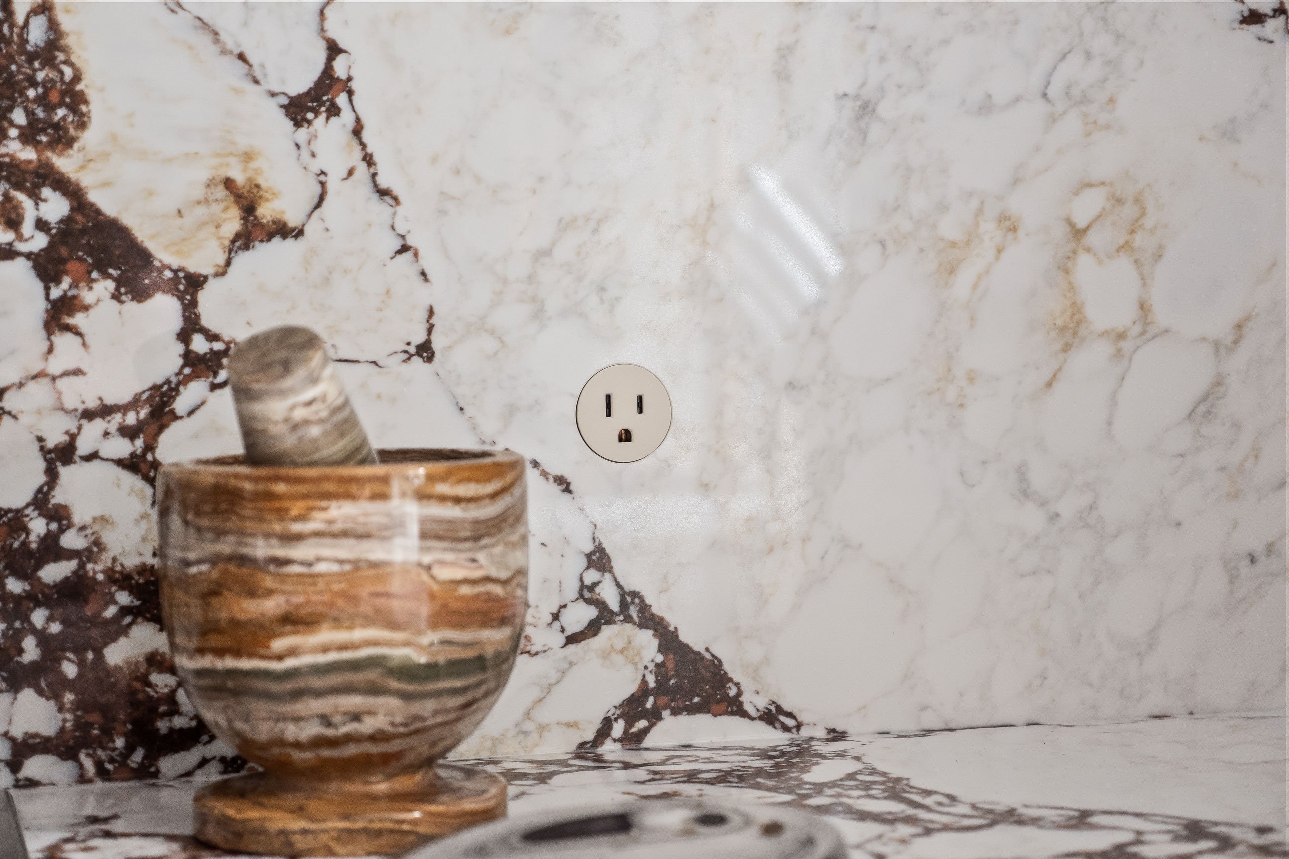A color-matched electrical outlet built discreetly into the stone backsplash beside a stone mortar and pestle.