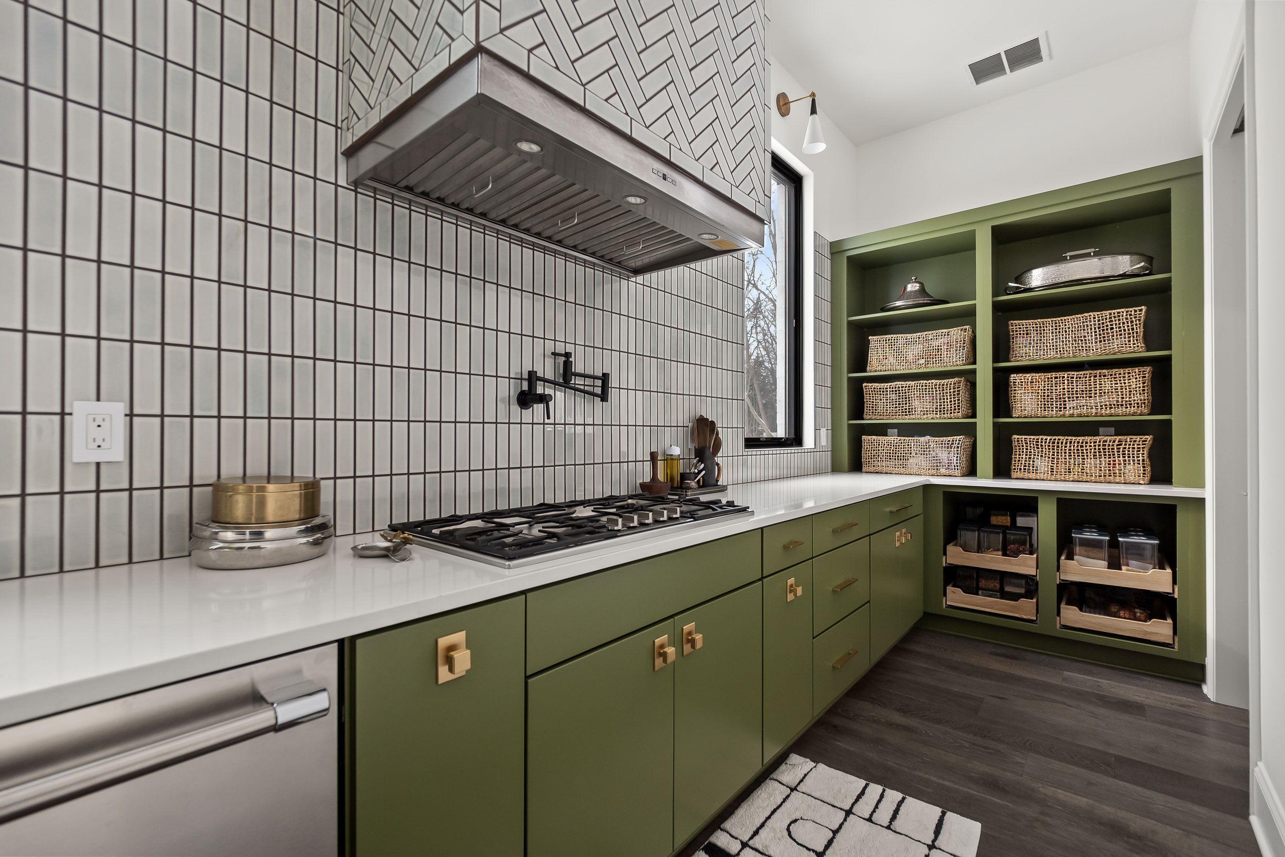 Secondary kitchen counter with olive green cabinetry, light quartz countertop, vertical gray tile backsplash and black faucet.