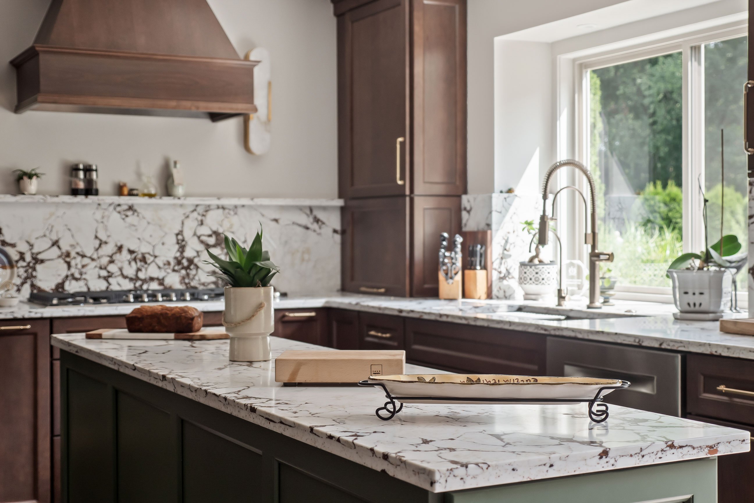 Wide view of the island countertop with a loaf of banana bread and serving dishes, sink and window visible beyond.