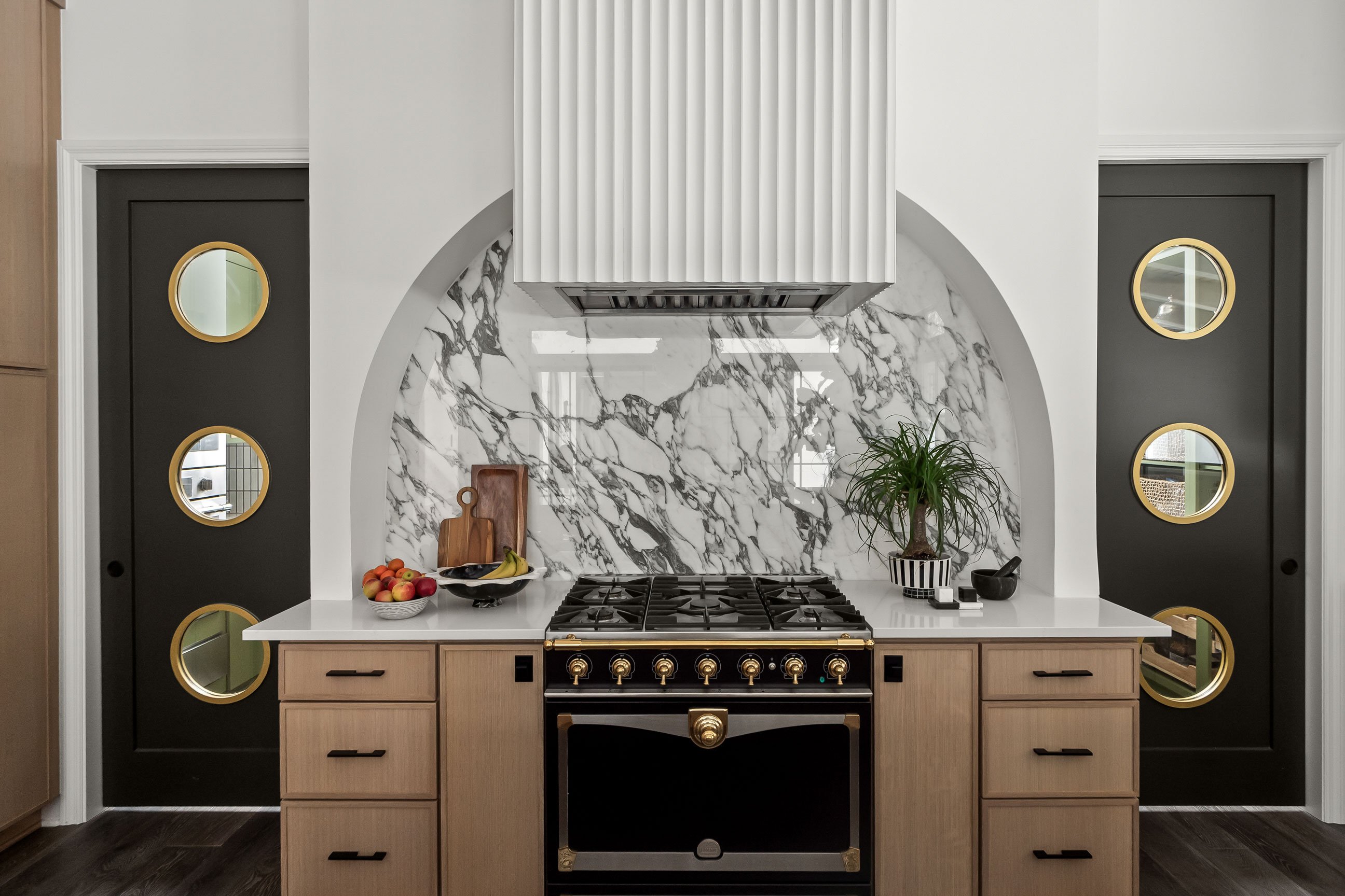 Modern kitchen with large quartersawn white oak cabinets, waterfall island with dramatic veined countertop, black metal pendant lights and mixed metal accents.