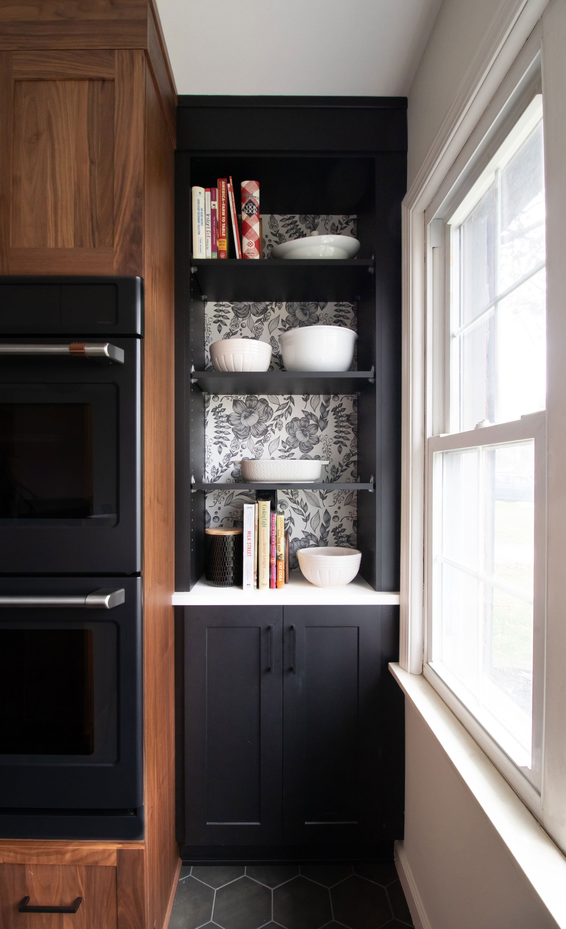 Inspira Cabinetry in natural walnut with black painted cabinetry niche featuring contrasting floral wallpaper