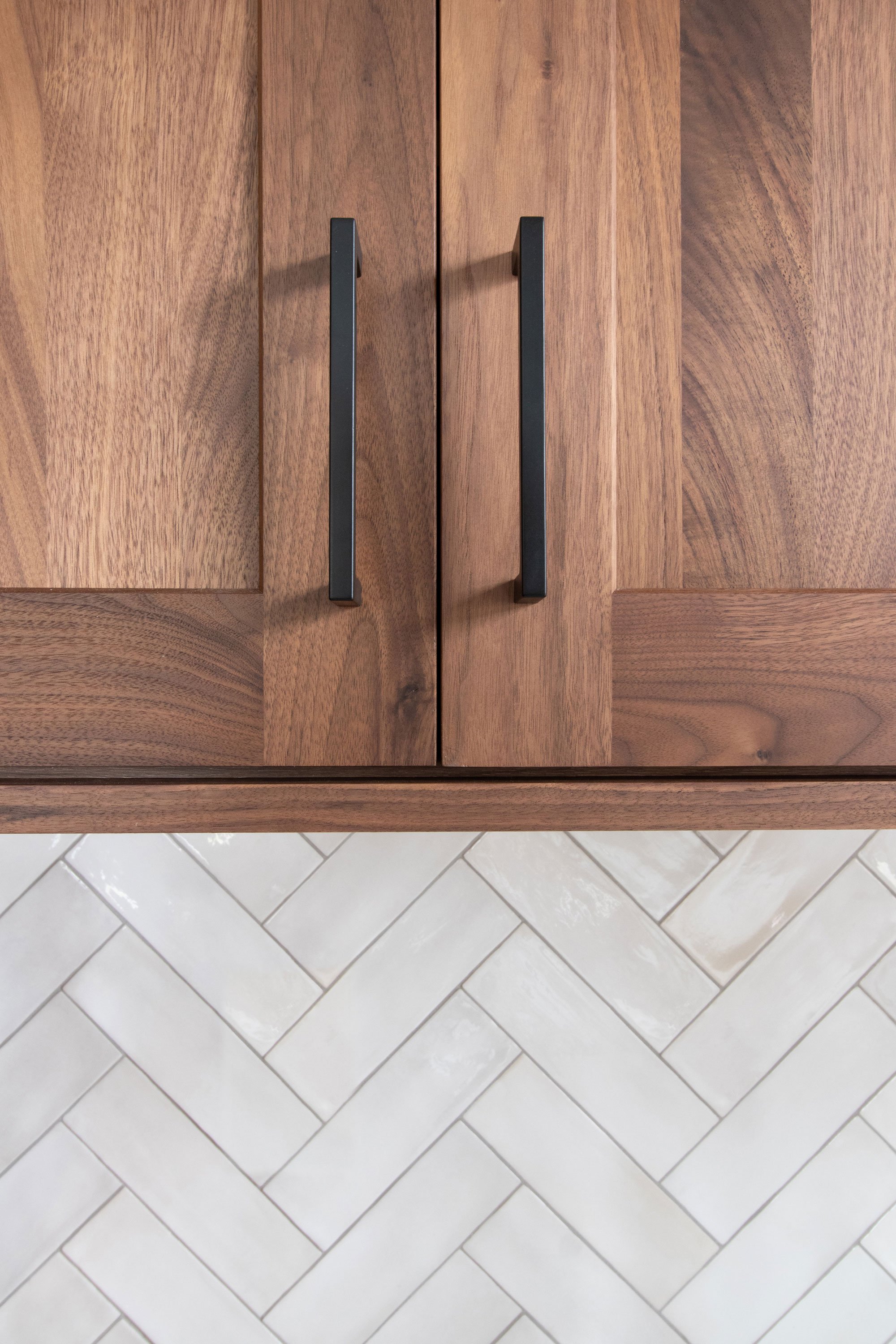 Inspira Cabinetry in natural walnut with matte black hardware and white herringbone tile backsplash