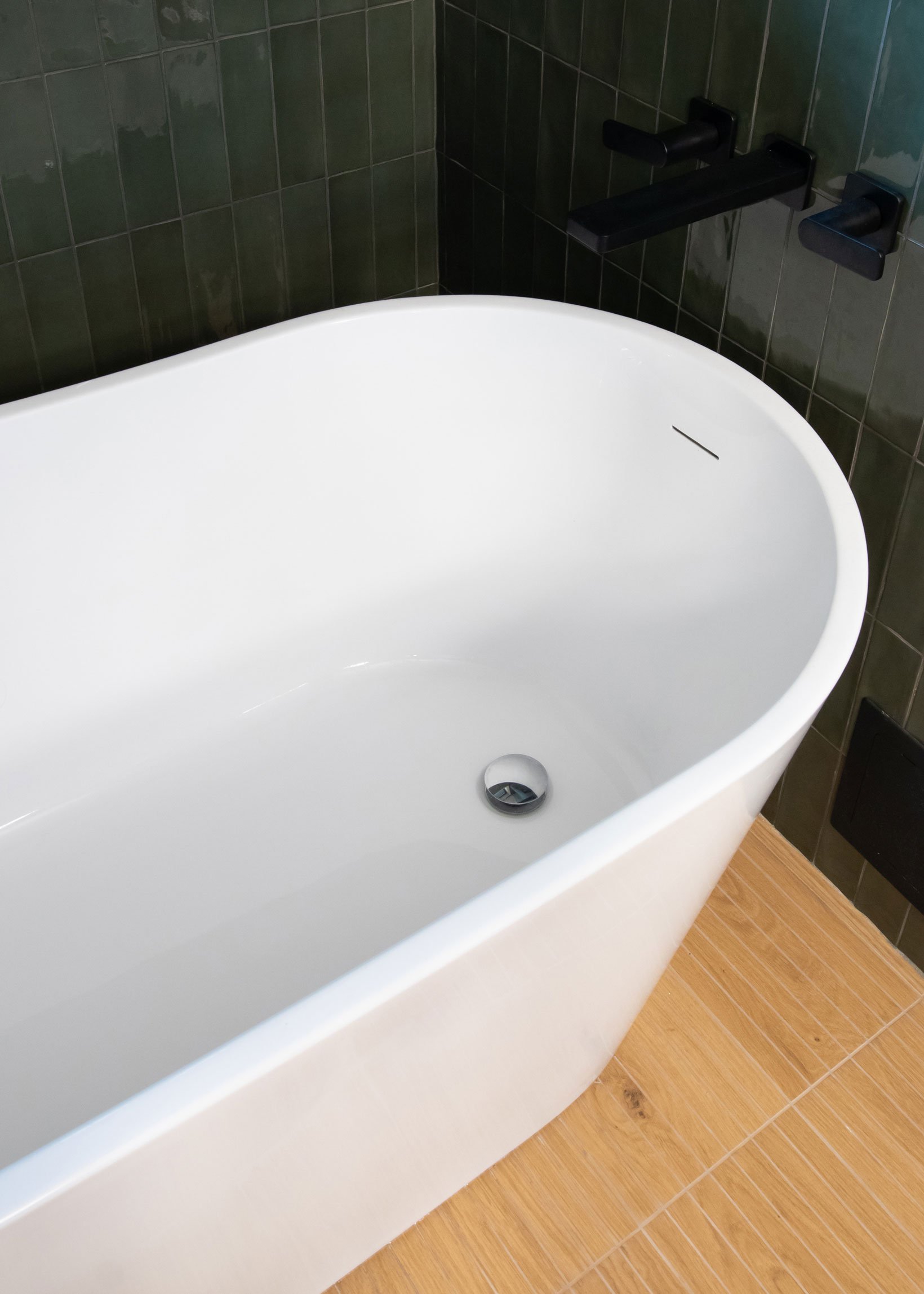 Freestanding tub with green tile surround and warm flooring