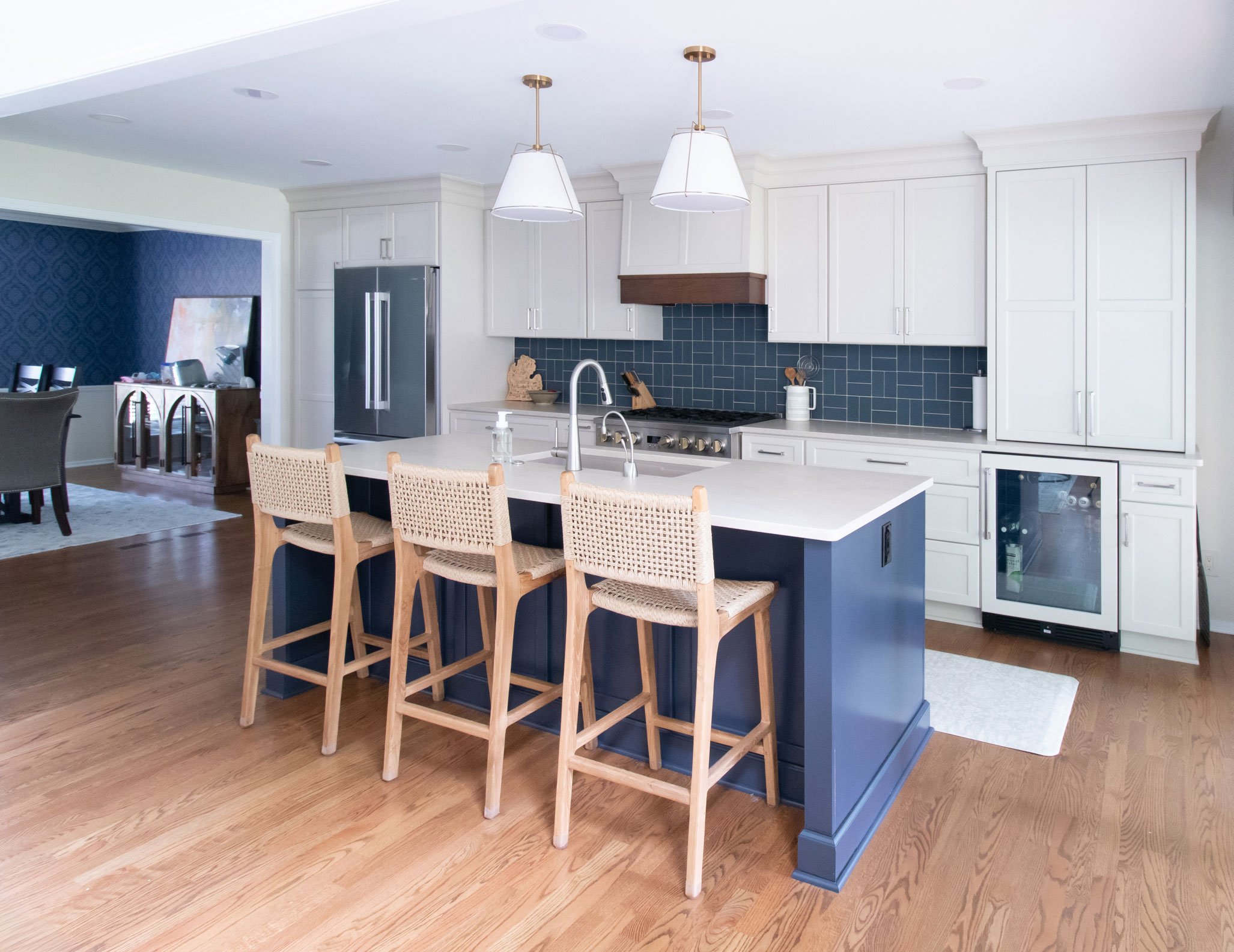 Open kitchen renovation featuring a navy island, custom white cabinetry, blue backsplash tile, and expanded floor plan.