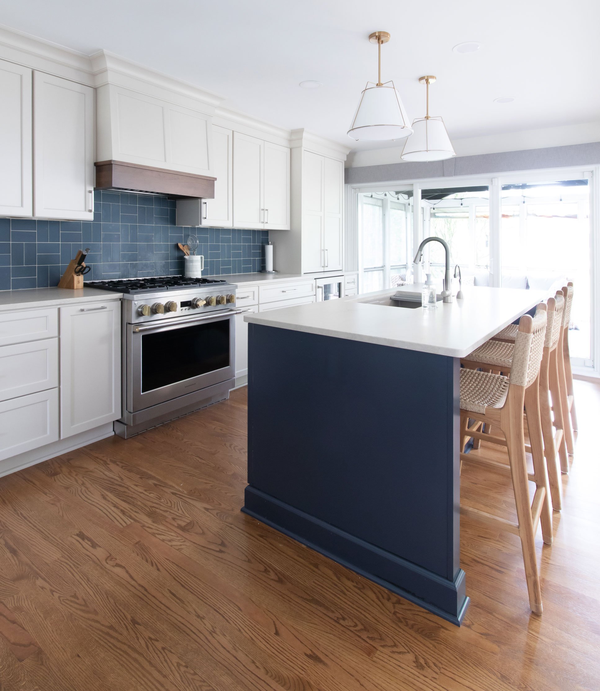 Large navy blue island with seating overlooking a custom kitchen with white cabinetry, wood hood, and professional-style range.