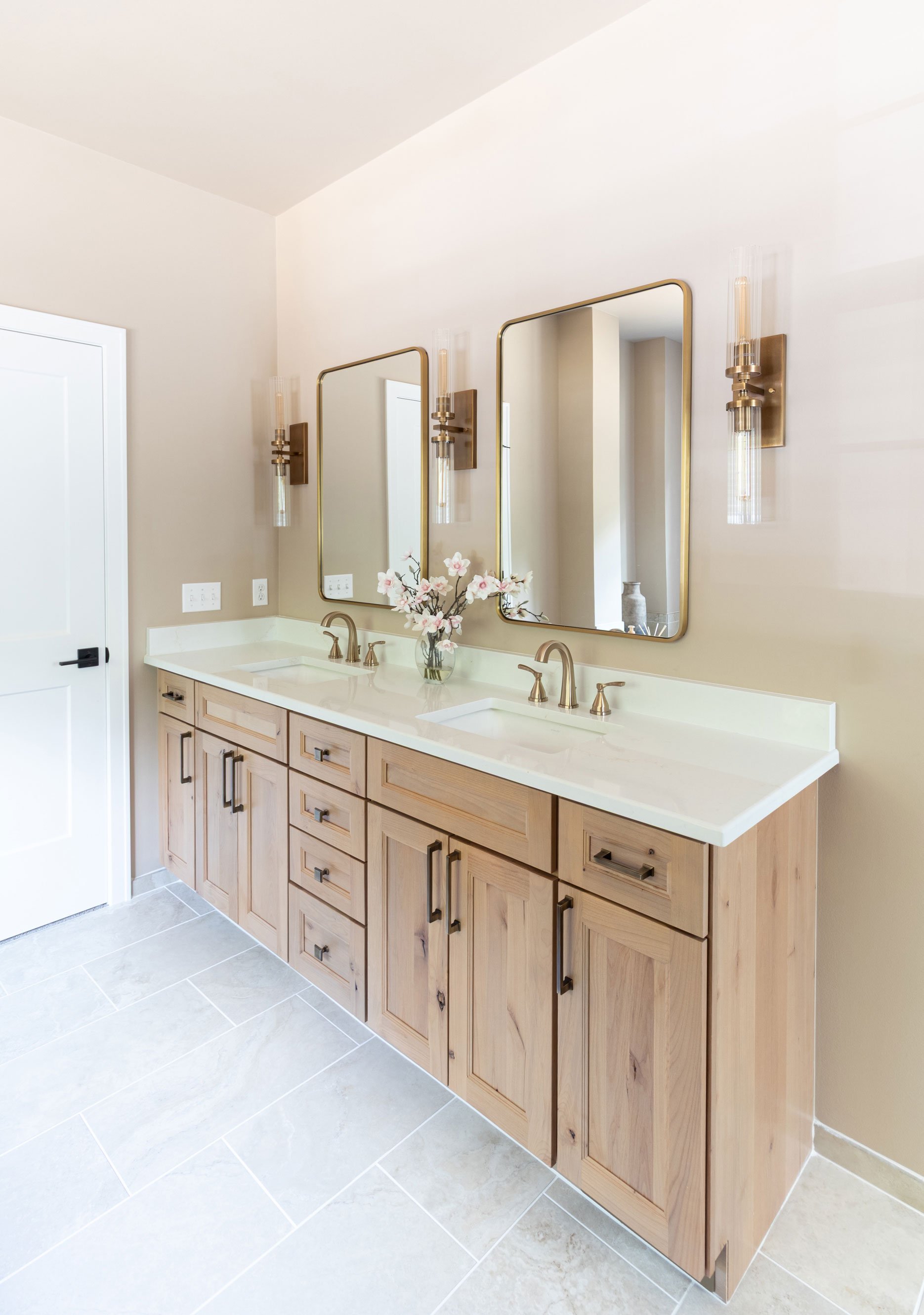 The master bathroom double vanity viewed from an angle, showing the Studio Beige cabinetry, brass fixtures, and paneled mirrors above the quartz counter.