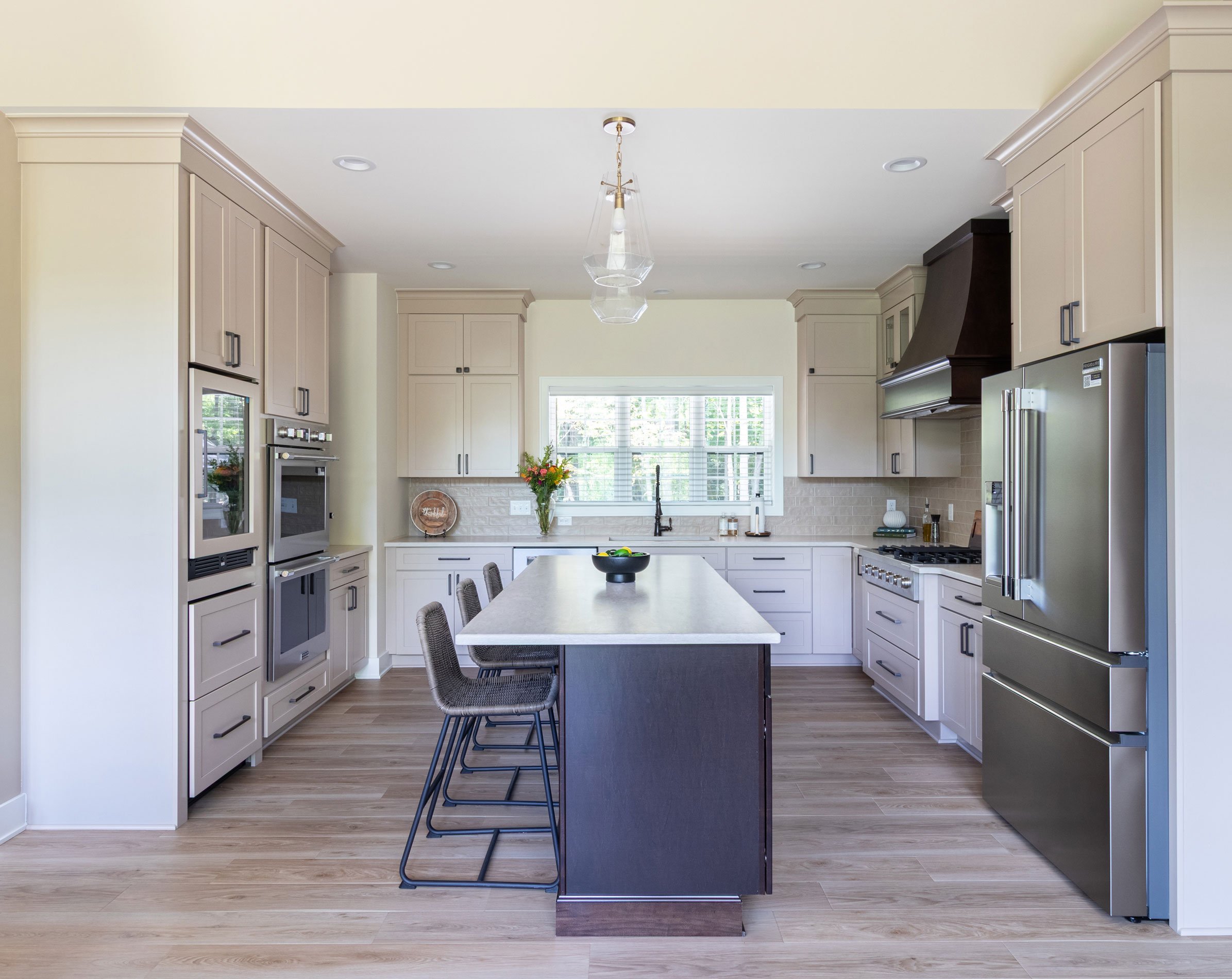 A new-build kitchen with Studio Beige perimeter cabinetry, a Maple Peppercorn island, dark accent range hood, and stainless appliances.