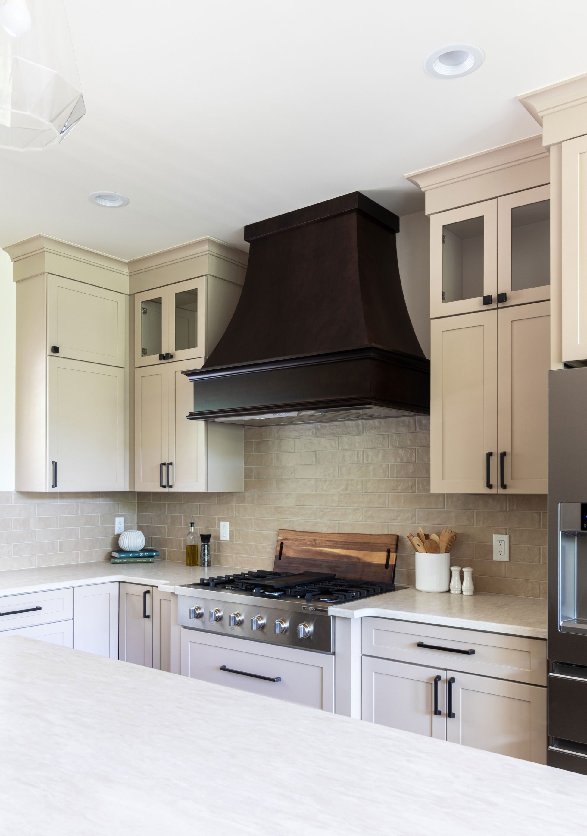 The range wall with a Maple Peppercorn accent hood set against tiled backsplash and Studio Beige flanking cabinetry.