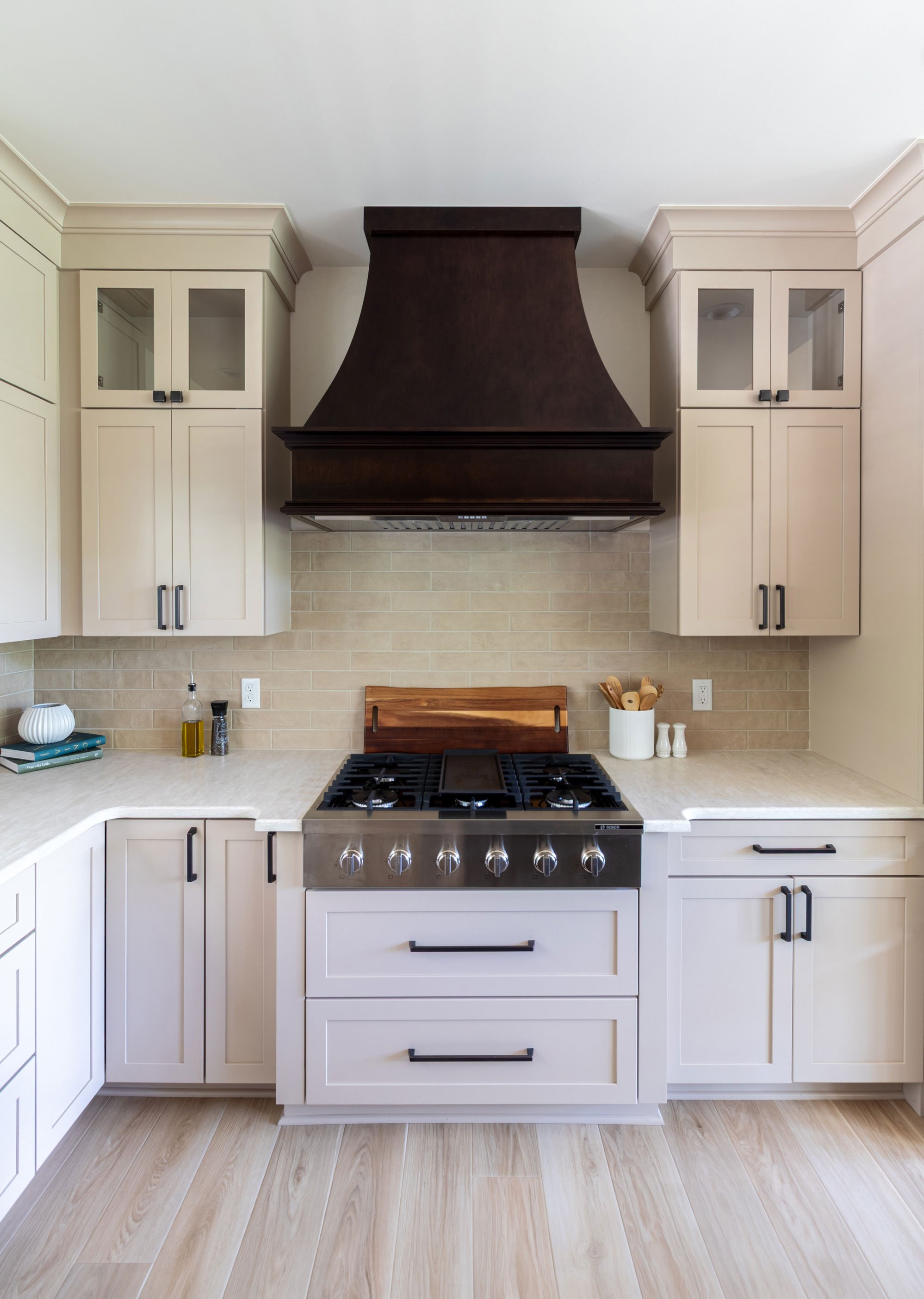 Straight-on view of the Maple Peppercorn range hood above the gas cooktop and tile backsplash.