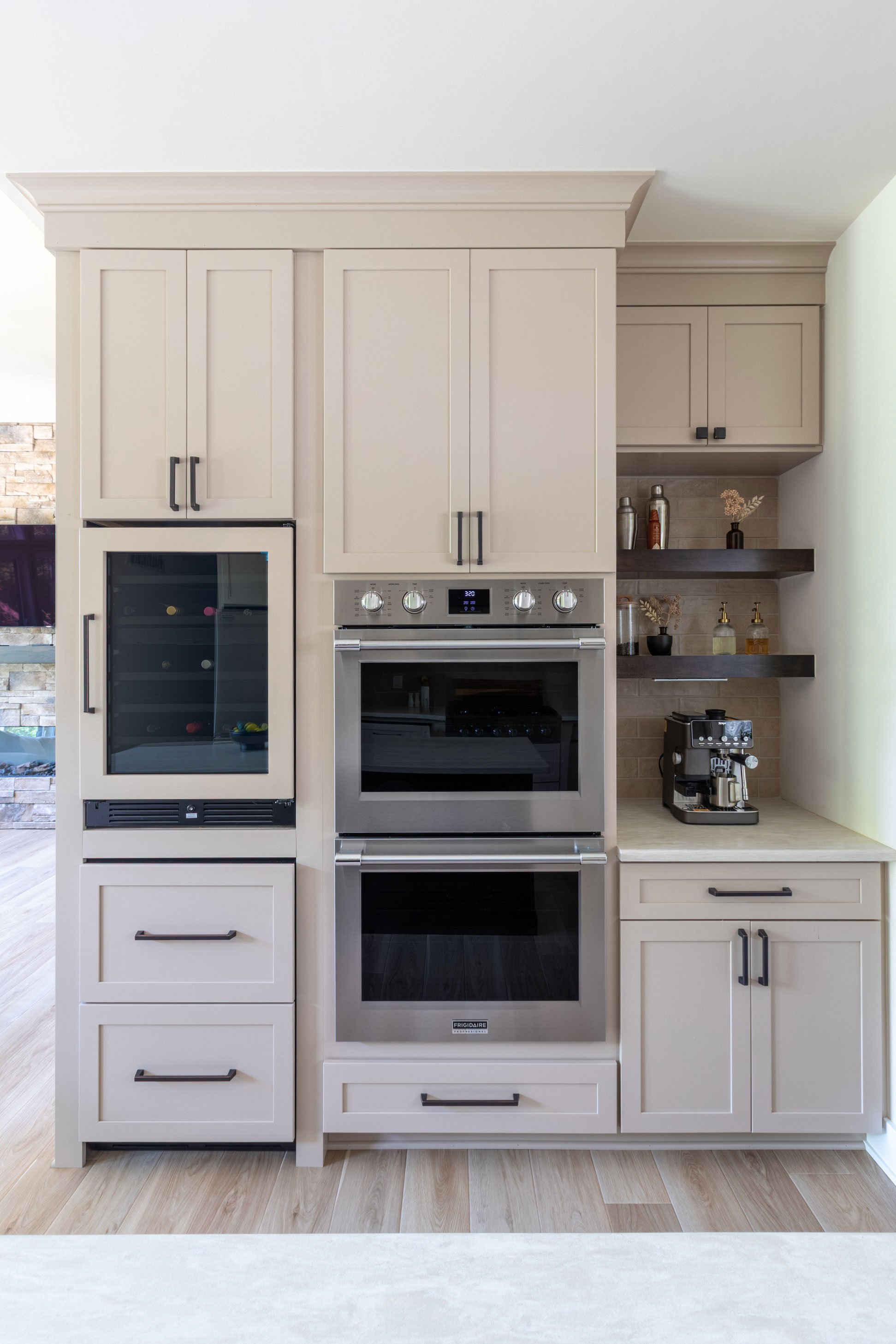 Straight-on view of the oven tower and coffee bar, showing the panel-front wine refrigerator, double ovens, and open shelving.