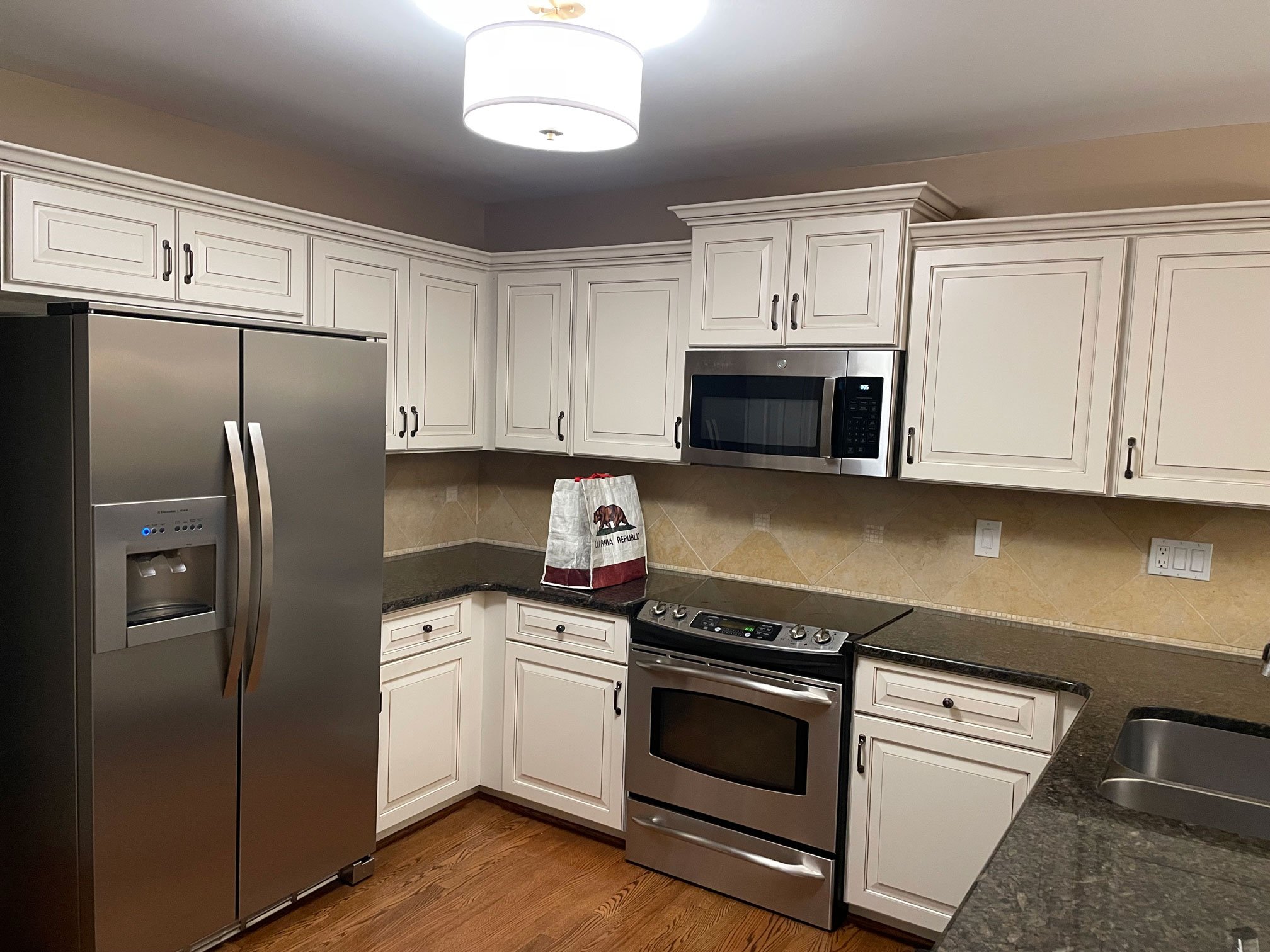 Traditional U-shaped kitchen featuring white raised-panel cabinets, dark countertops, stainless steel appliances, and tile backsplash.