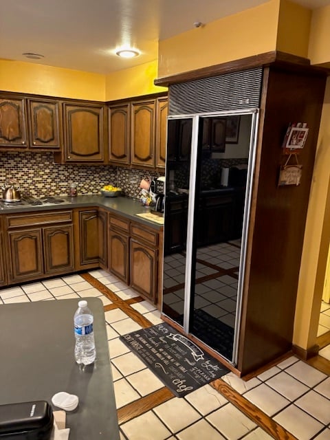 A corner of the original kitchen showing a mirrored built-in refrigerator, mosaic tile backsplash, and tile flooring prior to renovation.