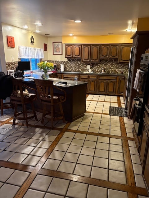 A wider view of the original kitchen with peninsula and no island, featuring dark wood cabinetry, dated lighting, and tile flooring before the remodel.