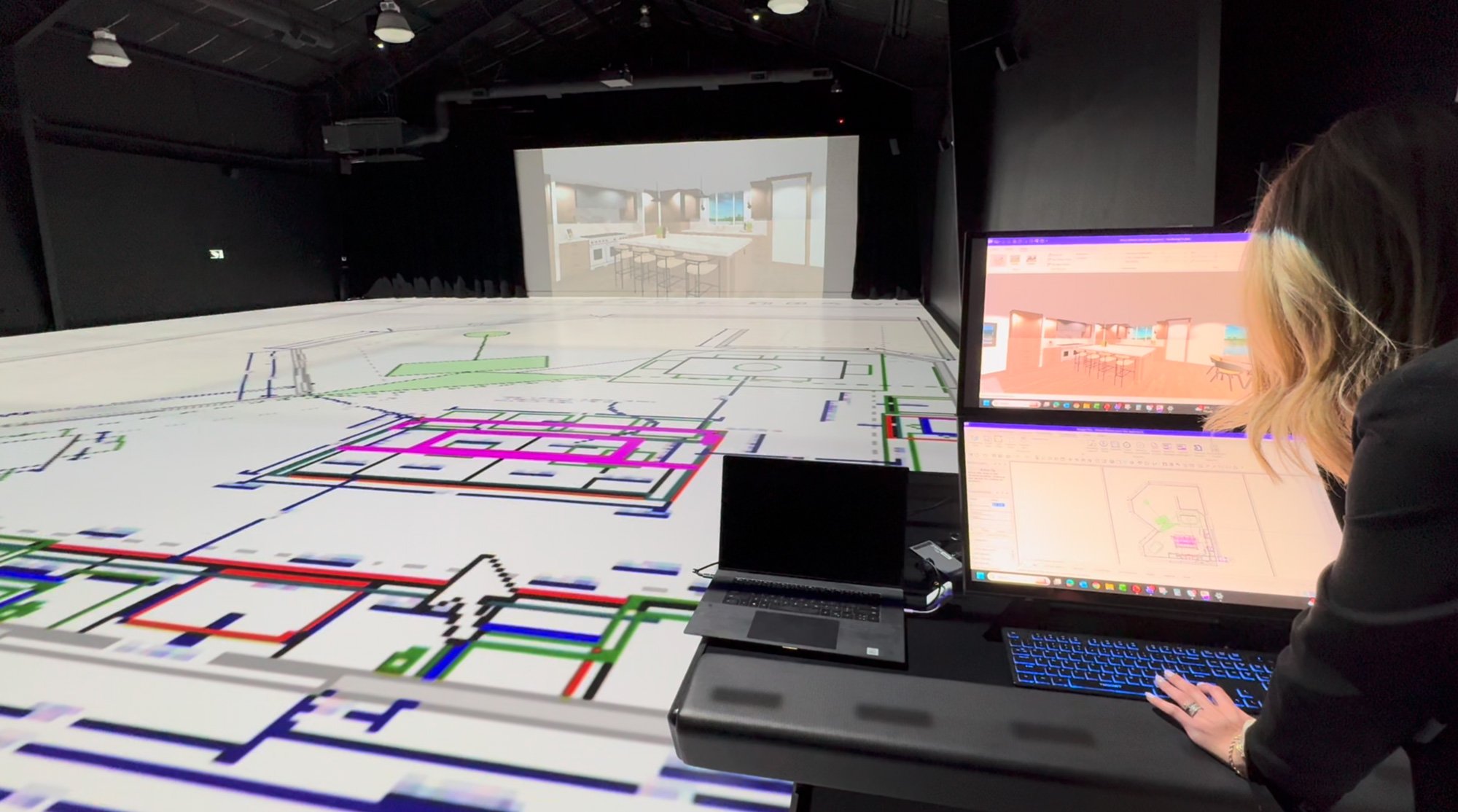 Sandra Daubenmeyer uses live design software controls at TrueScale Studio while a full-scale projected floor plan and kitchen rendering update in real time.